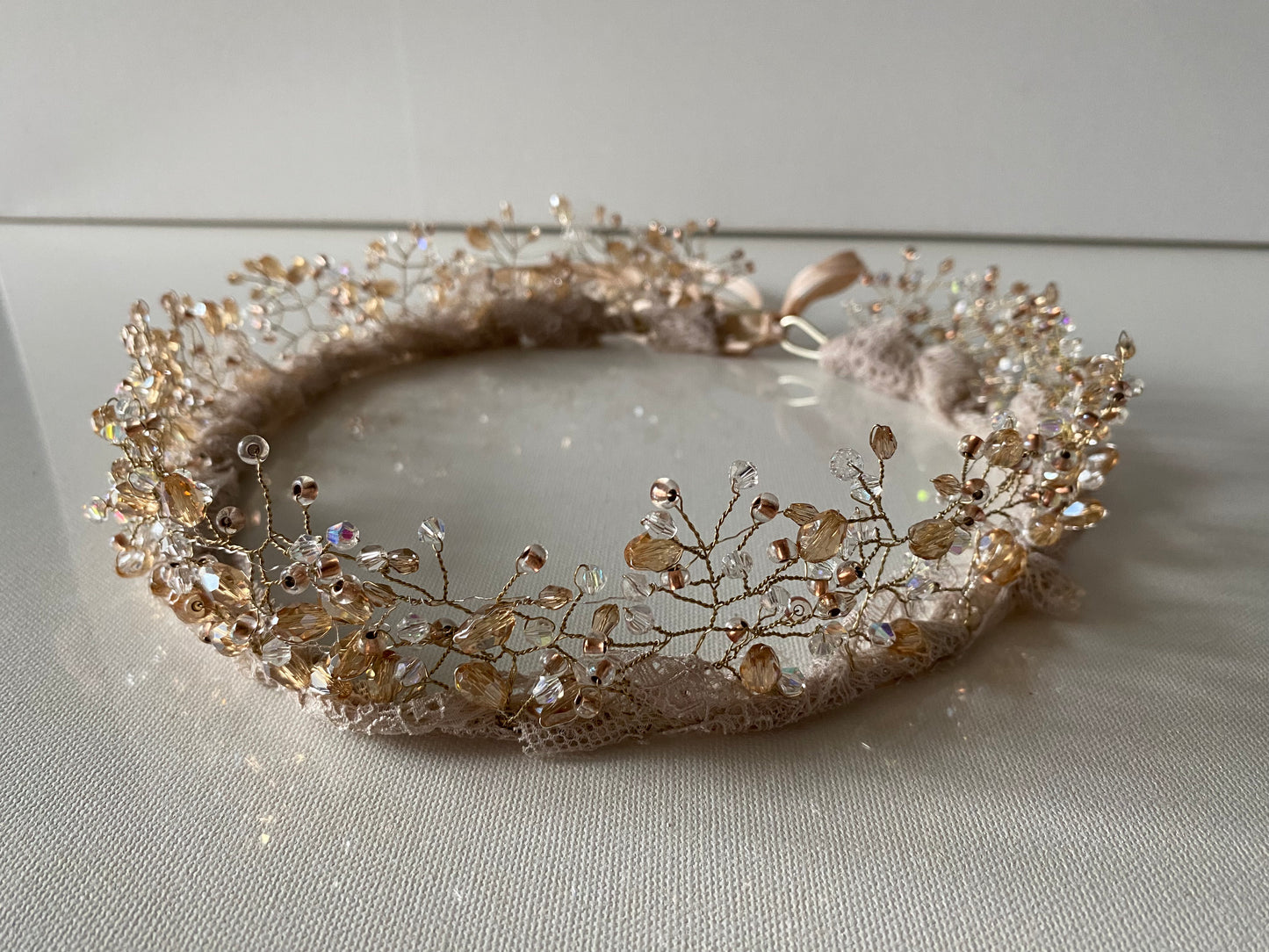 Stikla pērļu kronis baltos, bēšos un caurspīdīgos toņos ar mežģīnes apdares pamatni bēšā krāsā, sasienams