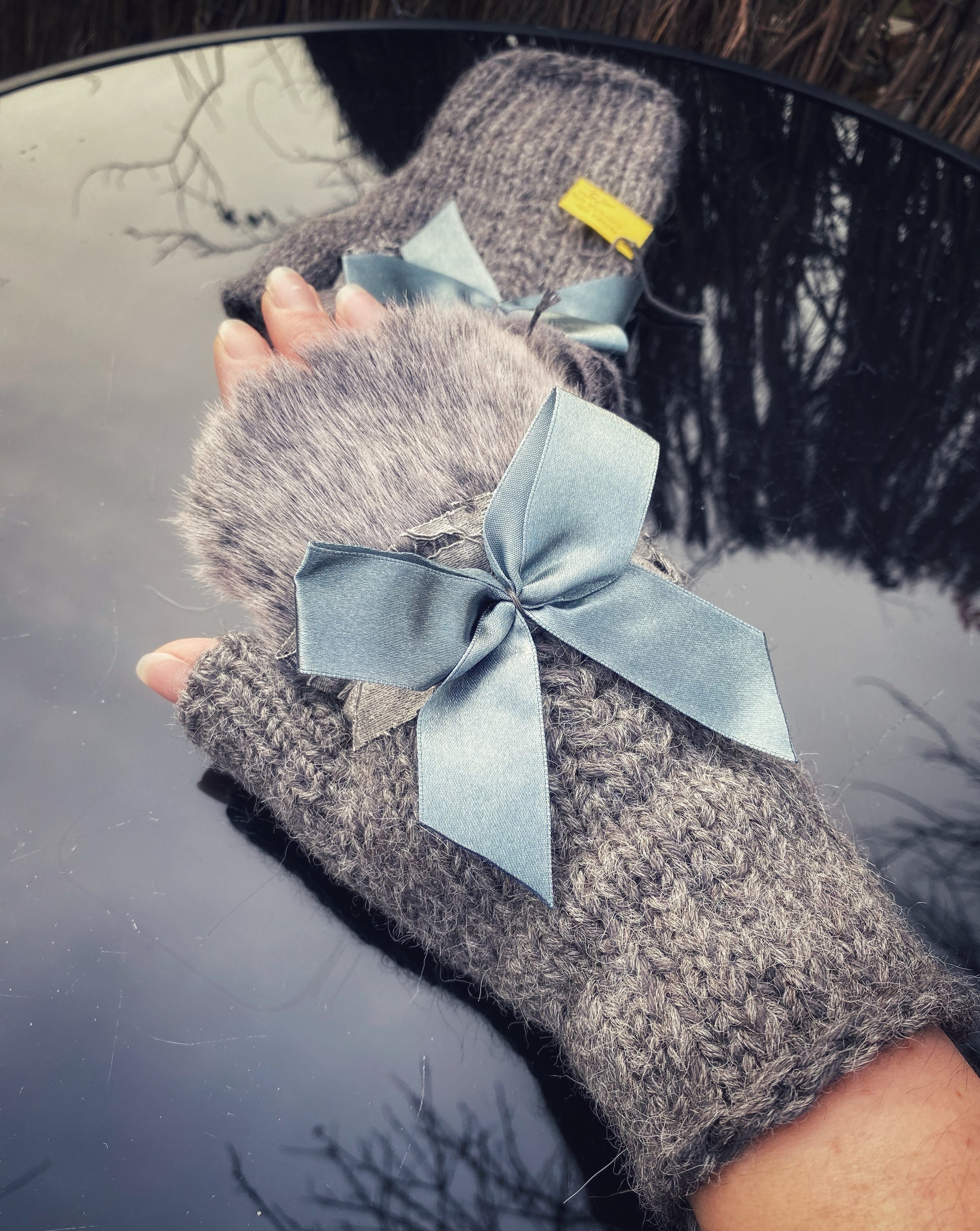 Pieaugušo puscimdiņi ar anatomisko īkšķi, no pelēkas alpakas dzijas ar mākslīgās kažokādas dekoru un atlasa banti